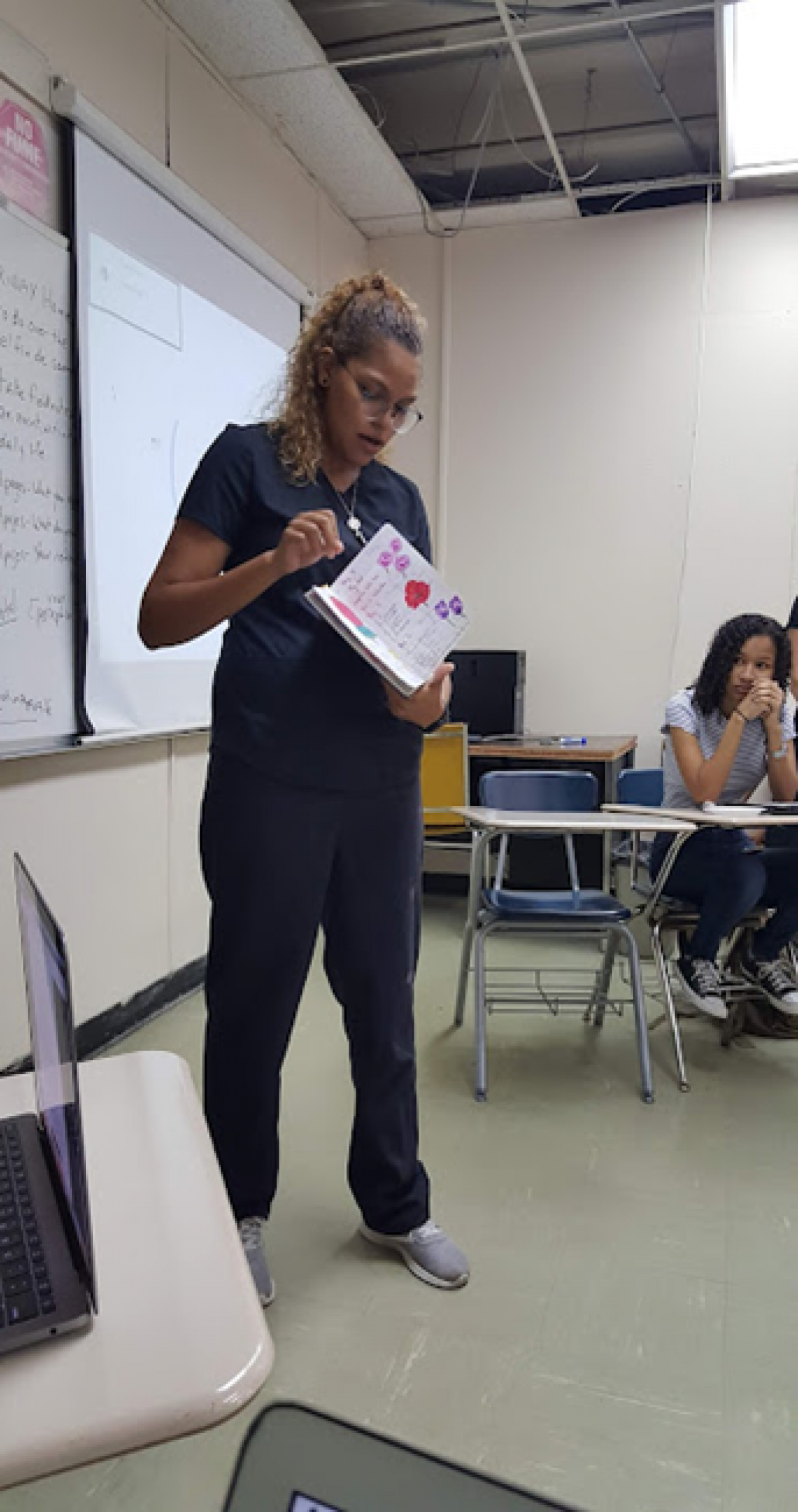 student presenting in front of class holding a notebook